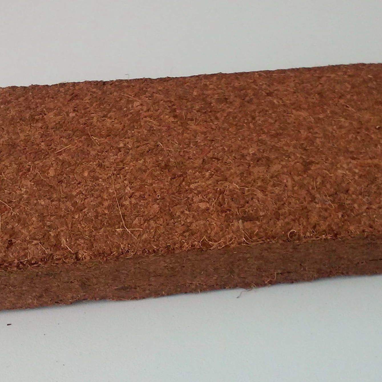 A compressed brick of reddish-brown coco peat, fine particles with a few short fibers, on a plain pale surface.