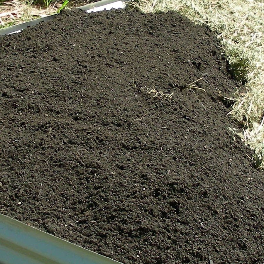Dark, finely crumbled blended soil spread across a new vegetable bed, with straw along one edge.
