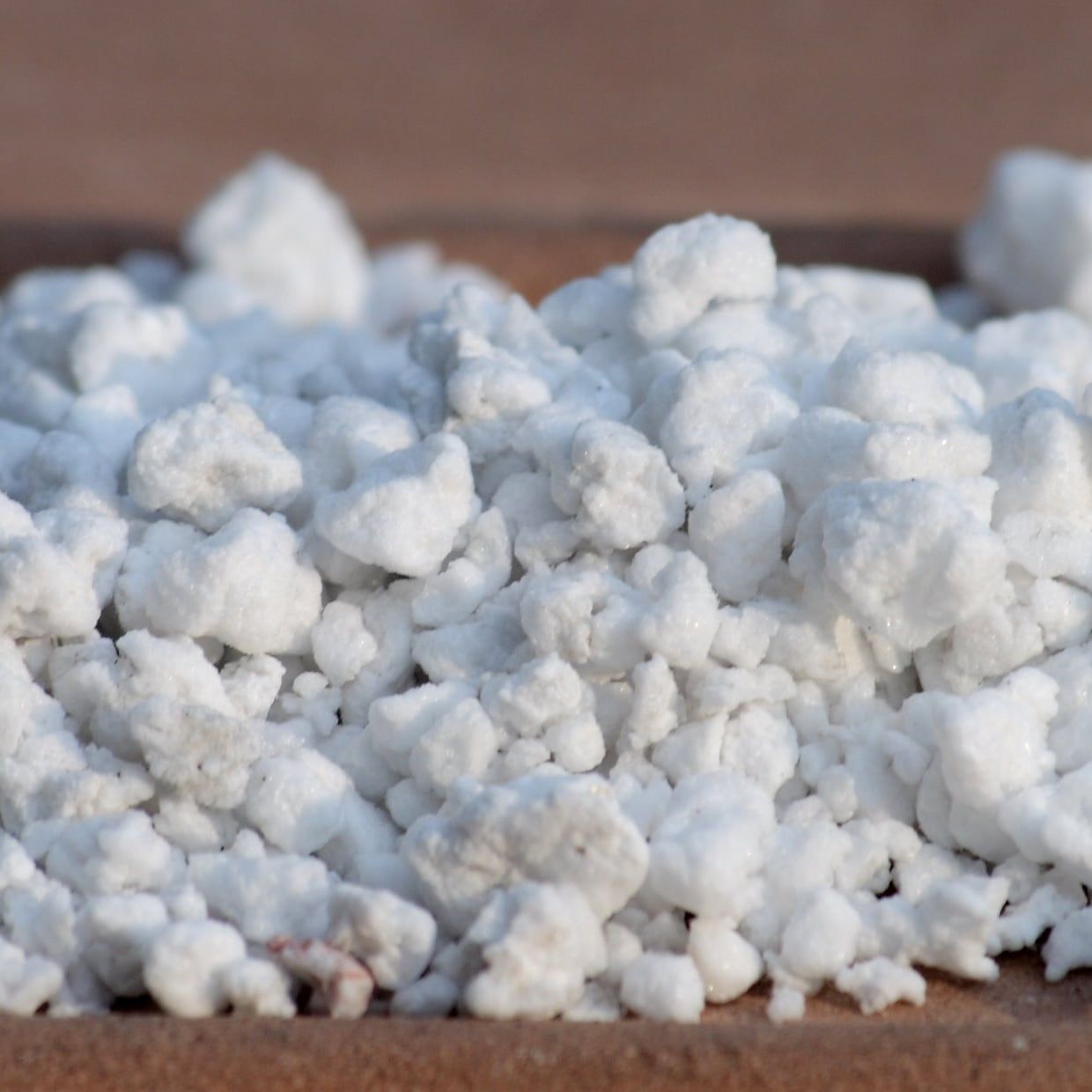 A heap of white, irregular horticultural perlite granules on a wooden board.